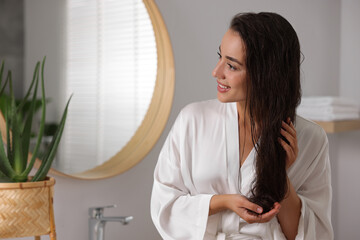 Young woman applying cosmetic hair mask in bathroom. Space for text