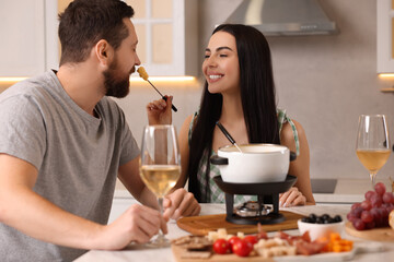 Affectionate couple enjoying cheese fondue during romantic date in kitchen