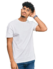 Young arab man wearing casual white t shirt confuse and wondering about question. uncertain with...