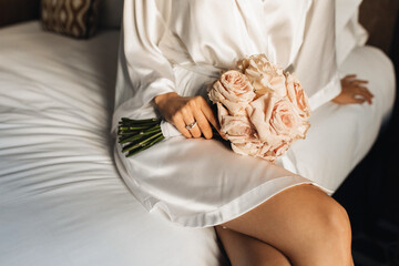 A close-up photo of the bride's luxurious bouquet in her hands with a wedding ring. The girl holds a bouquet of roses before the wedding