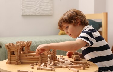 Cute little boy playing with wooden construction set at table in room. Child's toy