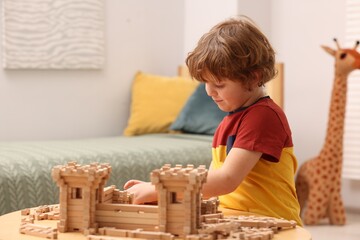 Fototapeta na wymiar Cute little boy playing with wooden construction set at table in room. Child's toy