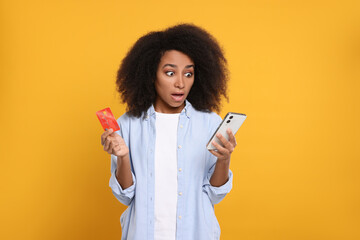 Shocked woman with credit card and smartphone on orange background. Debt problem - obrazy, fototapety, plakaty