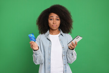 Confused woman with credit card and smartphone on green background. Debt problem