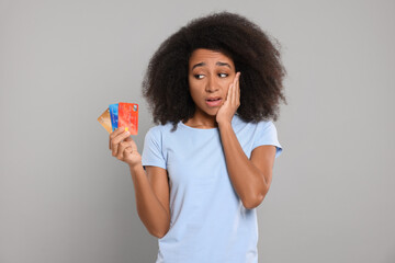 Confused woman with credit cards on grey background. Debt problem