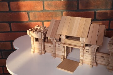 Wooden gate on white table near brick wall. Children's toy