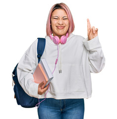 Hispanic woman with pink hair wearing student backpack and headphones gesturing finger crossed smiling with hope and eyes closed. luck and superstitious concept.