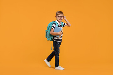 Happy schoolboy in glasses with backpack and books on orange background