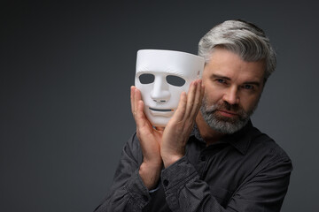 Multiple personality concept. Man with mask on dark grey background, space for text
