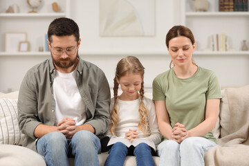 Girl and her godparents praying together on sofa at home