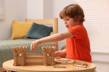 Cute little boy playing with wooden construction set at table in room. Child's toy
