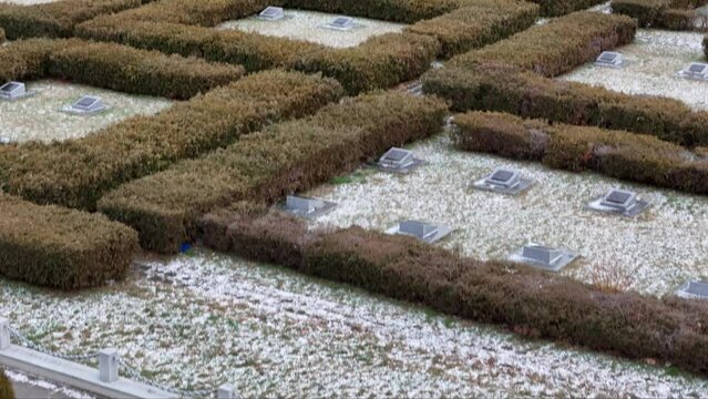 Bird's-eye perspective of a snowy, orderly WWII cemetery, with a monument marking the unspoken atrocities of the war.