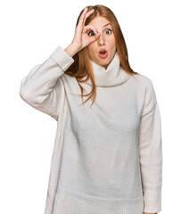 Young irish woman wearing casual winter sweater doing ok gesture shocked with surprised face, eye looking through fingers. unbelieving expression.