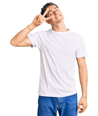 Young handsome man wearing casual white tshirt doing peace symbol with fingers over face, smiling cheerful showing victory