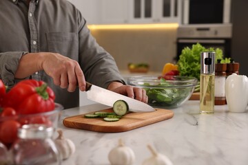 Obraz na płótnie Canvas Cooking process. Man cutting fresh cucumber at white marble countertop in kitchen, closeup