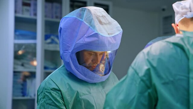 Mid-aged Caucasian doctor is wearing the full protection uniform. Surgeon working at trauma surgery in modern hospital.
