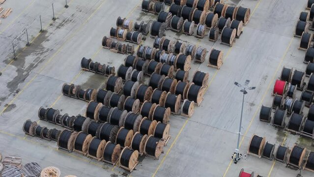 View from above showcases wooden cable drums laid out in organized rows at an outdoor warehouse. Cloudy drone footage.