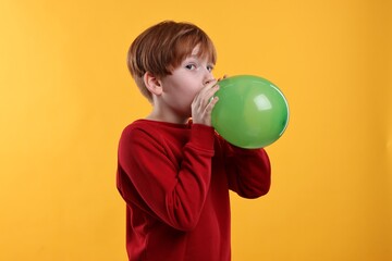 Boy inflating green balloon on orange background