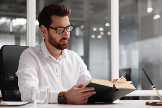 Handsome man reading book at table in office, space for text. Lawyer, businessman, accountant or manager