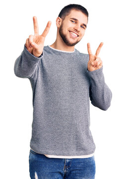 Young handsome man wearing casual sweater smiling looking to the camera showing fingers doing victory sign. number two.