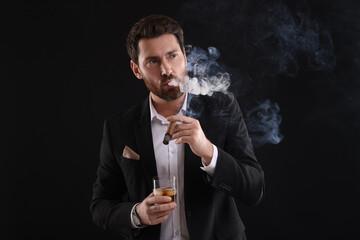 Handsome man in elegant suit with glass of whiskey smoking cigar on black background