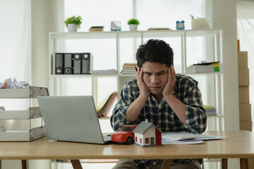 A young Asian man is stressed about bills, car payments, house payments, and holds his head in his...