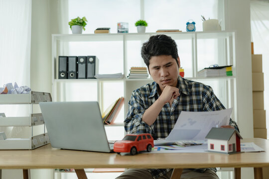 Young Asian man calculates car payments Home installments in financial planning and income Asset approval concepts, buying cars and houses, checklist, home loans, home taxes