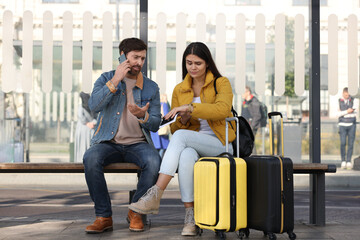 Being late. Worried couple with suitcases sitting at bus station outdoors