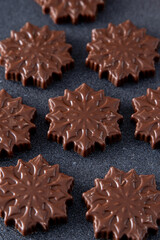 Chocolate candies in the shape of snowflakes. Brown food background.