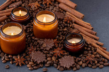 Soy scented candle in a jar. Coffee beans, anise, cinnamon spices. The candles are burning. Dark background