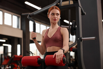 Fototapeta premium Athletic young woman training with lat pulldown machine in gym