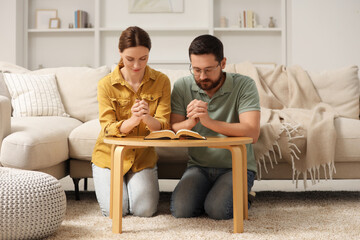 Family couple praying over Bible together at table indoors