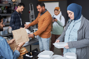 Side view of Middle Eastern young woman wearing headscarf receiving hot meal at refugee help center...