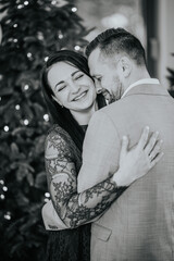  black and white photo of a laughing couple embracing, with a Christmas tree in the background.