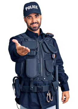 Young hispanic man wearing police uniform smiling cheerful offering palm hand giving assistance and acceptance.