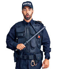 Young hispanic man wearing police uniform holding baton scared and amazed with open mouth for...