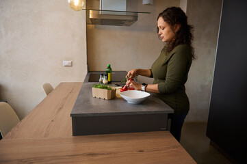 Charming body positive young woman standing at kitchen table, sorting ingredients while cooking healthy dinner at home