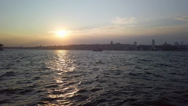 Evening, cinematic slow-mo, sun setting over Istanbul Kadikoy, casting Bosphorus in a golden hue. The scene features captivating view of the Bosphorus as the camera glides past waterfront railings.