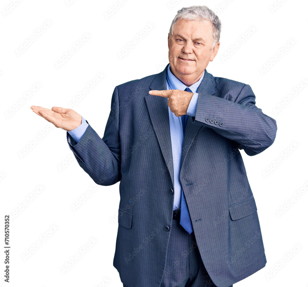 Wall mural Senior grey-haired man wearing business jacket amazed and smiling to the camera while presenting with hand and pointing with finger.