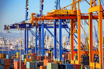 Naklejka premium A bustling cargo port with colorful containers, cranes, and shipping activity under a clear blue sky.