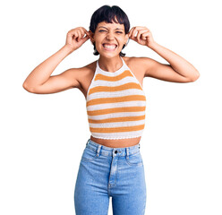 Young brunette woman with short hair wearing casual clothes smiling pulling ears with fingers,...