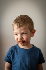 Retrato de niño rubio haciendo muecas con la boca sucia de chocolate