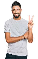 Young man with beard wearing casual grey tshirt smiling with happy face winking at the camera doing...