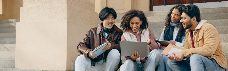 Cheerful students with laptop is studying outdoors sitting near university. Education concept