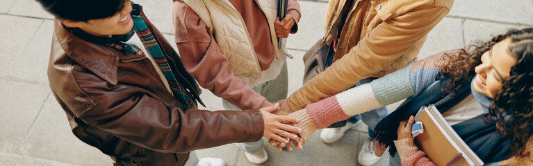 Top view of friendly young students putting their hands together standing near campus building