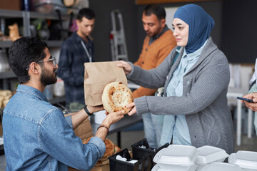 Side view portrait of Middle Eastern woman wearing headscarf receiving free food at refugee help...