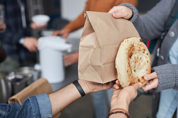 Close up of unrecognizable volunteer giving free food and bread to refugees at help center, copy...