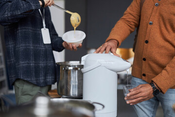Cropped image of unrecognizable people pouring hot drinks at soup kitchen or refugee help center, copy space