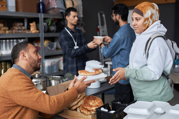Side view portrait of young Middle Eastern woman wearing headcover receiving free food and donations at refugee help center