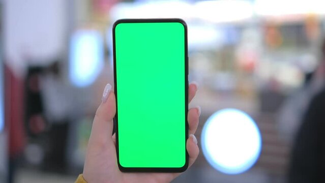 Use green screen for copy space closeup. Chroma key mock-up on smartphone in hand. Woman holds mobile phone and swipes photos or pictures in the mall 4K